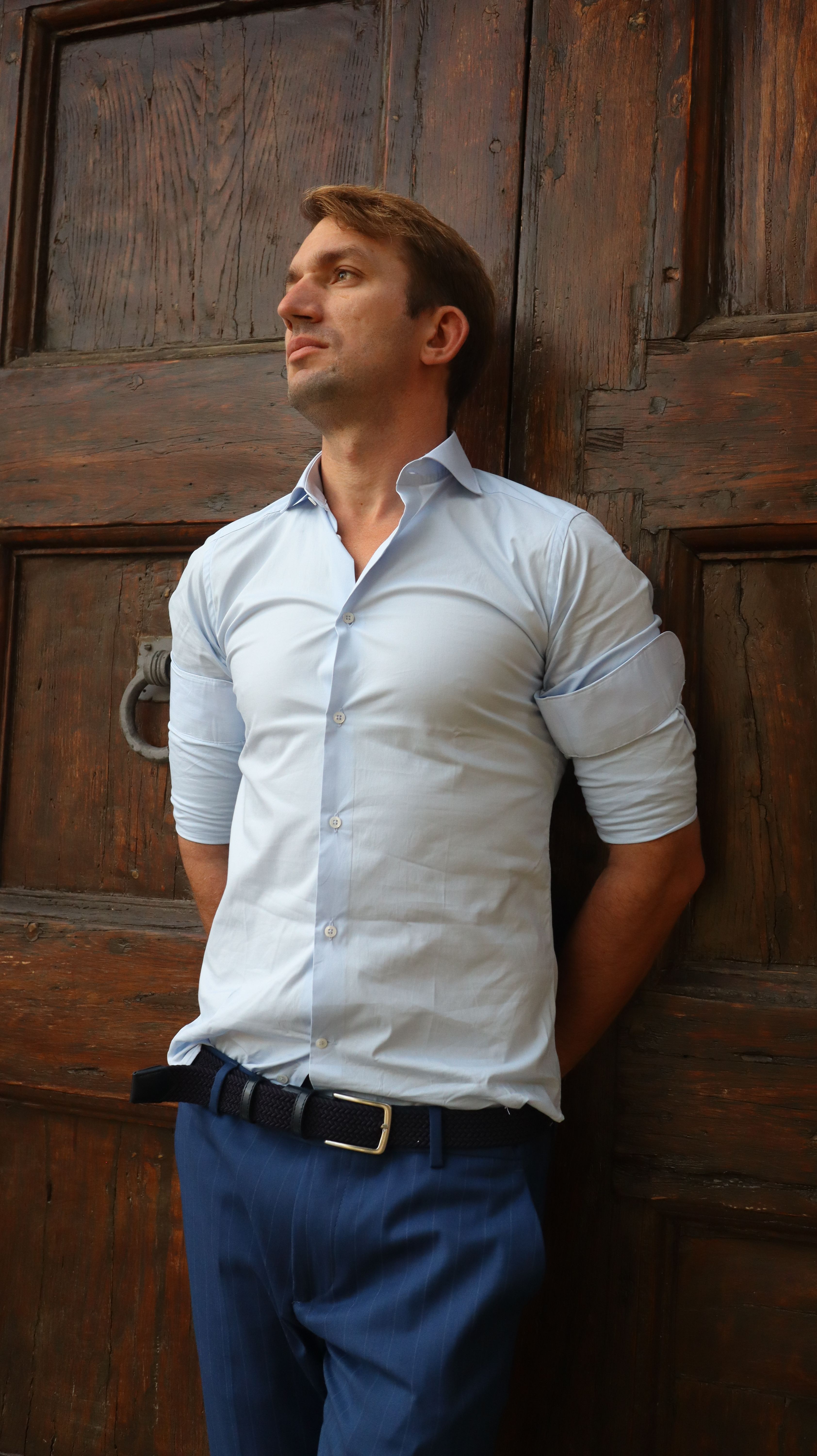 Elegant man in blue shirt posing confidently in front of a wooden door in Florence, Italy.
