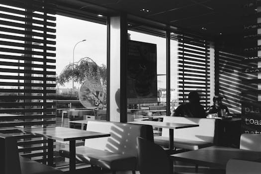 A monochrome view inside a McDonald's in Compiègne, showcasing empty seating and customers dining.