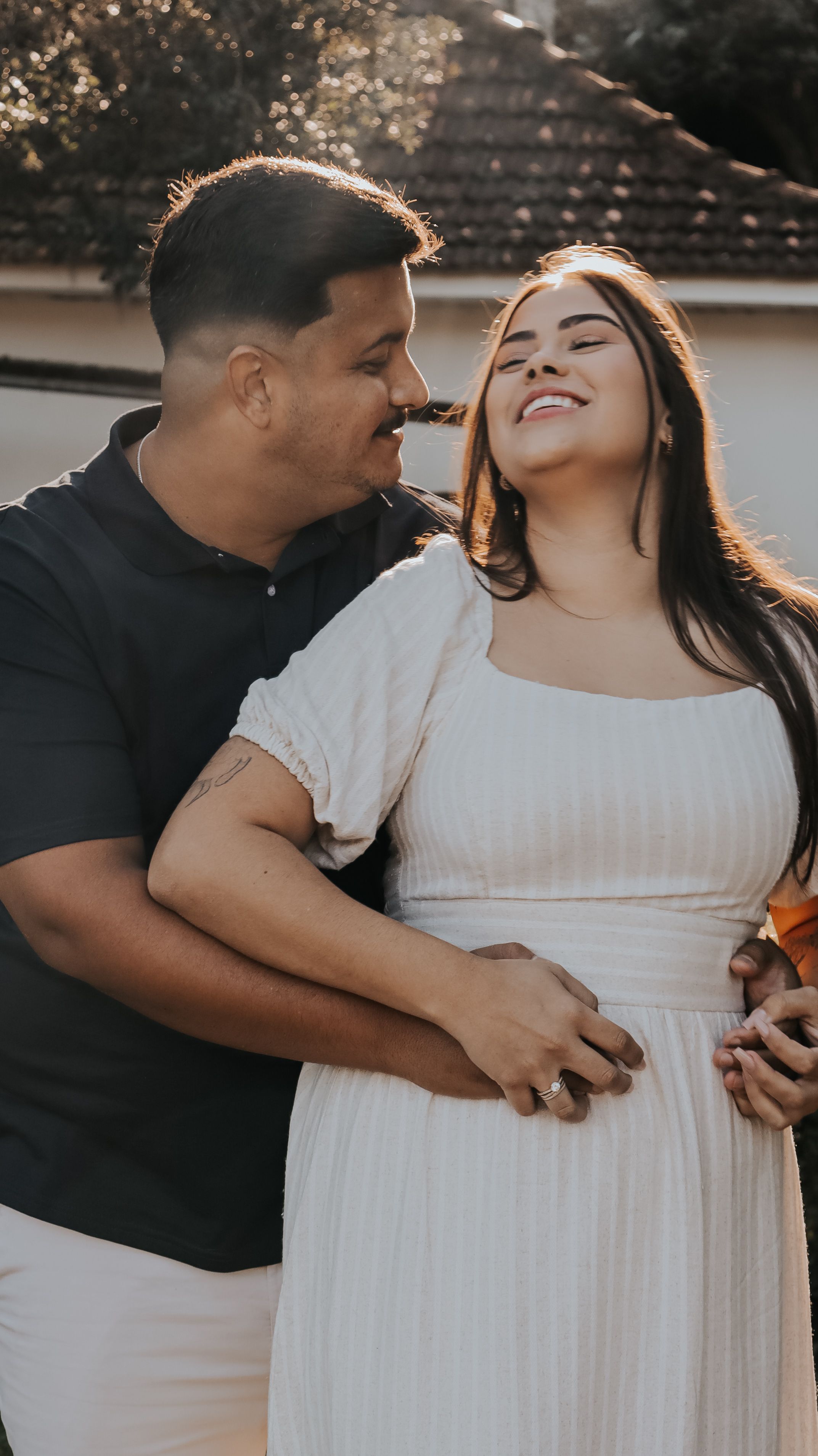 A joyful couple smiling and embracing outdoors under warm sunlight.