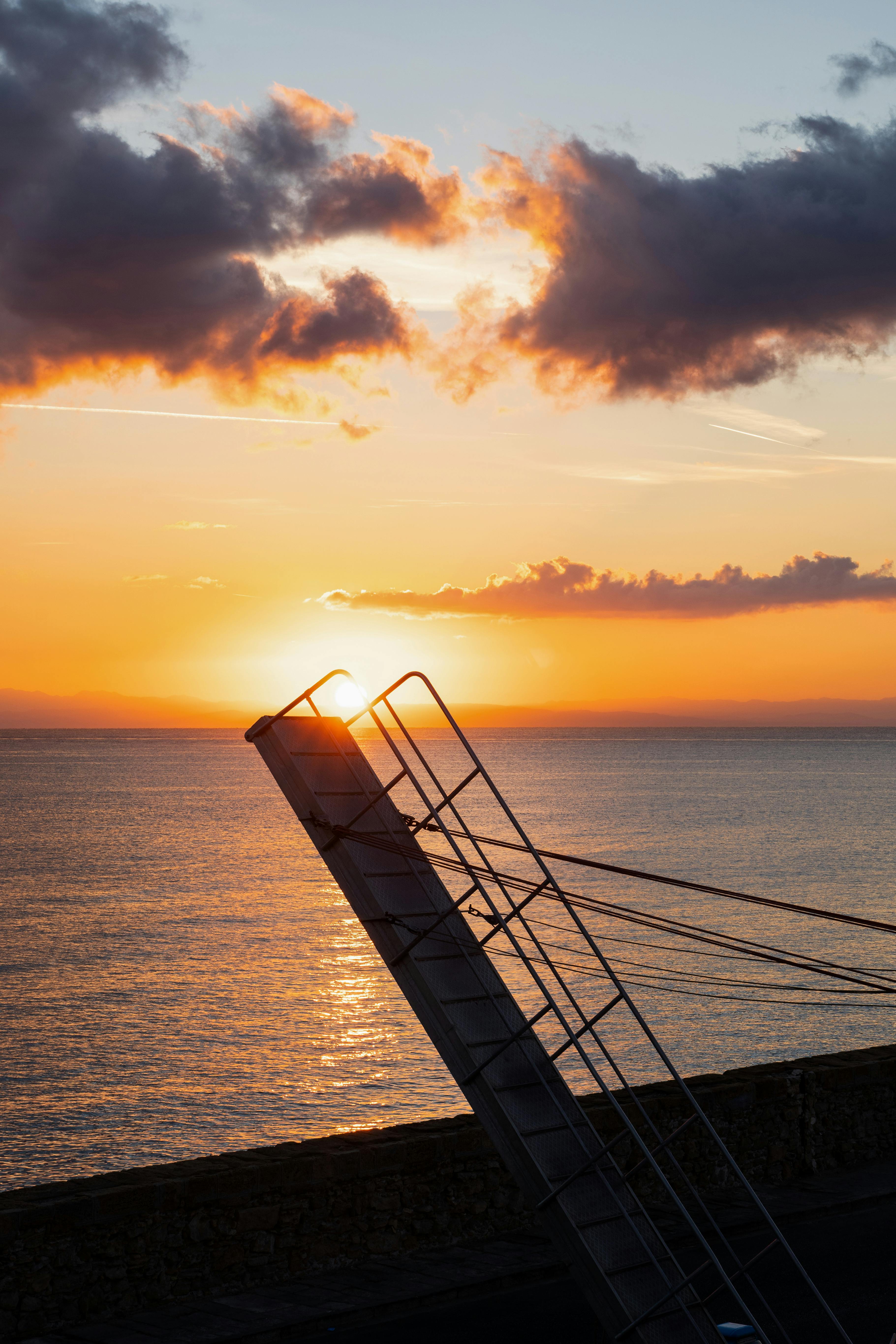 A tranquil sunset over the ocean, highlighted by a silhouetted structure, creating a vibrant coastal scene.