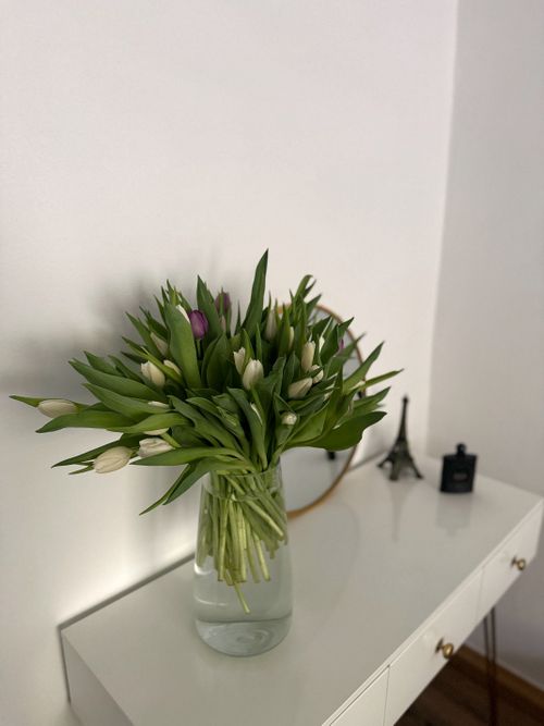 Free A bouquet of tulips in a glass vase on a white side table, enhancing minimalist decor. Stock Photo