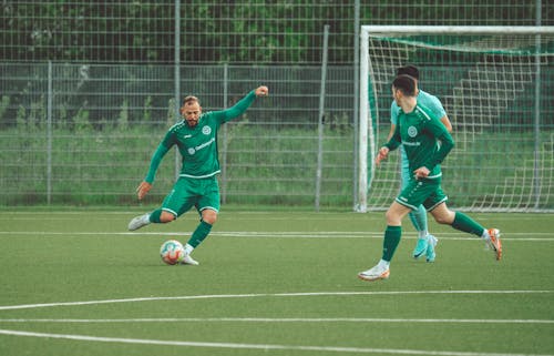 Two men in green uniforms playing soccer on a field