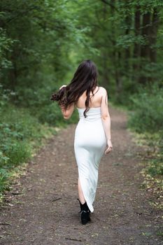 A woman in a white dress strolling through a serene forest path in summer.