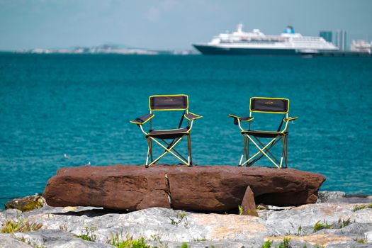 Two folding chairs overlooking the blue sea and distant cruise ship.