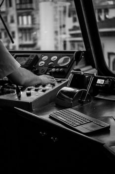 Black and white shot of a captain operating ferry controls, focus on levers and gauges.