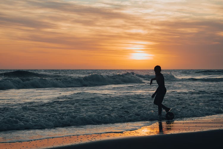 Silhouette Of Person Playing Ball On Beach At Dawn