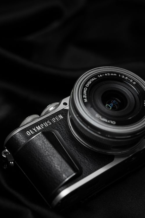 Free Close-up of an Olympus PEN digital camera with lens on a black fabric backdrop. Stock Photo