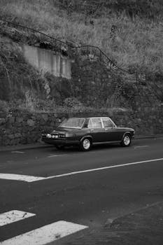 A classic car parked on a rural road in Madeira, Portugal. Black and white photograph.