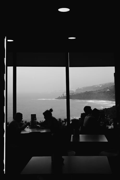 Black and white photo of people sitting at a table with the ocean in the background