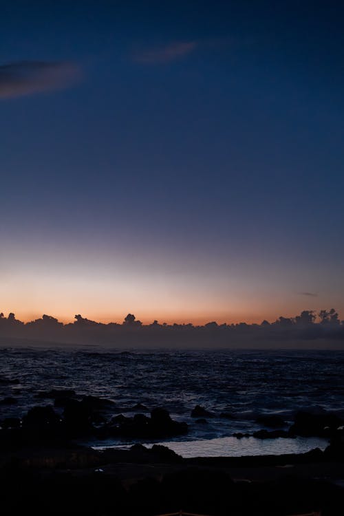 A sunset over the ocean with clouds and rocks