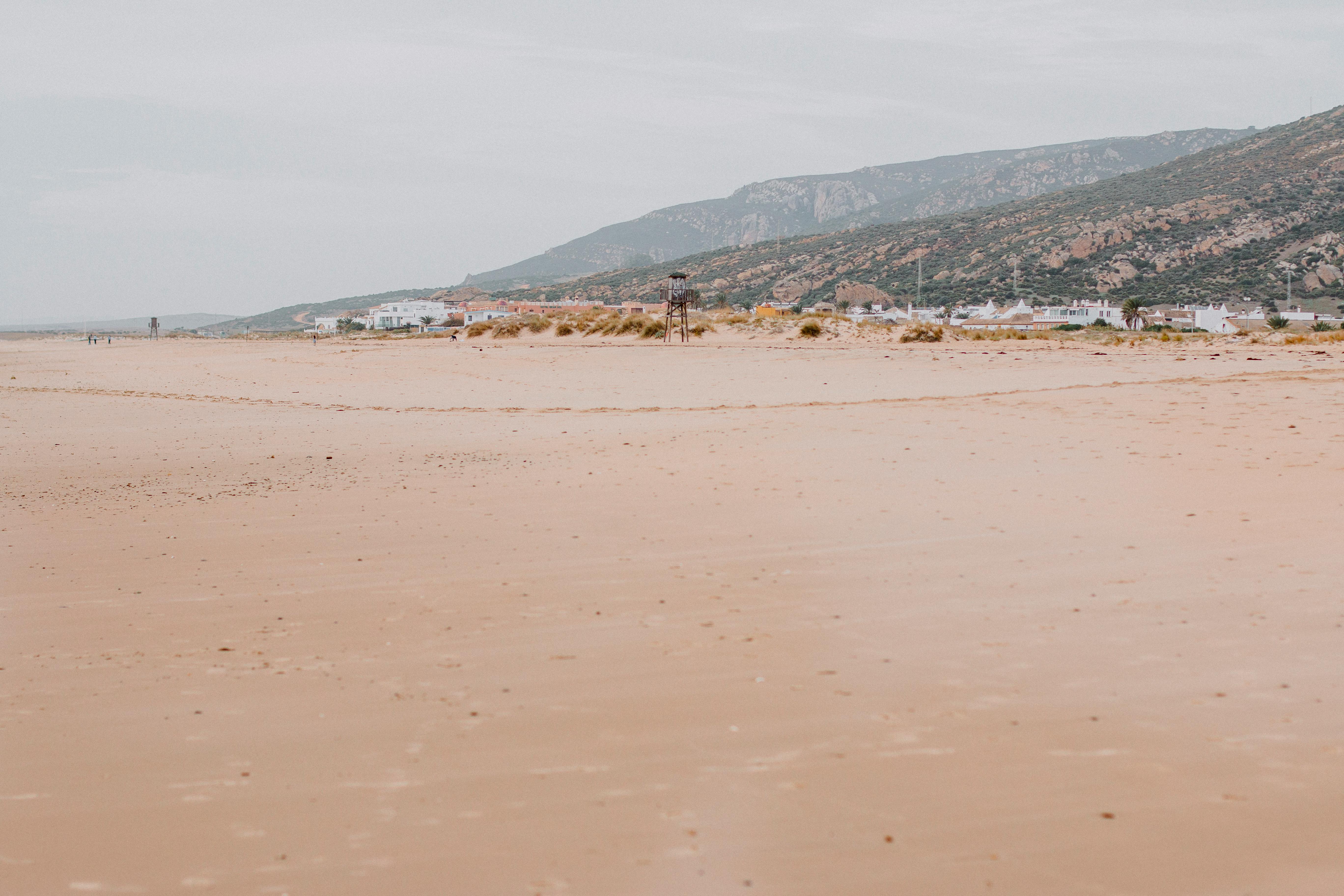 Peaceful sandy beach in Cádiz, Spain with distant hills and village.