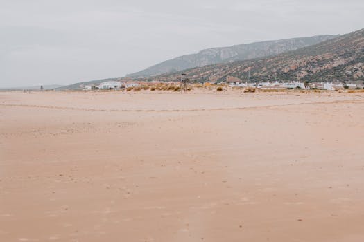 Peaceful sandy beach in Cádiz, Spain with distant hills and village.