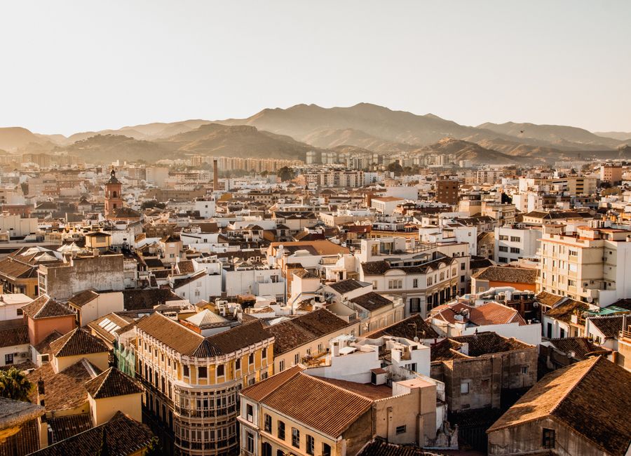 Aerial view of Málaga's cityscape with mountains in the background during sunset.