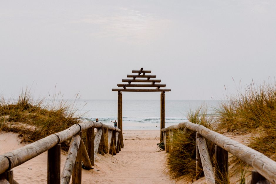 Wooden walkway through sand dunes leading to the tranquil shore in Cádiz, Spain.