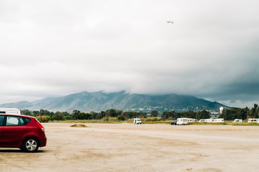 A picturesque view of the countryside in Málaga, Spain, featuring parked vehicles and dramatic cloud formations.
