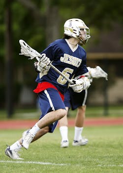 Dynamic image of a teenager playing lacrosse outdoors.
