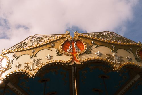 Free Close-up of an ornate carousel roof with intricate golden designs under a blue sky with clouds. Stock Photo