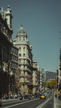 Street view of Barcelona with historic architecture, traffic, and pedestrians under a clear sky.