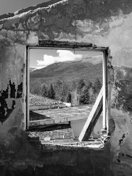 Black and white image of a mountain view through an abandoned building window in Oteshevo, North Macedonia.