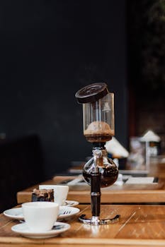 Vertical shot of a coffee syphon brewing in a café, with white cups and saucers.