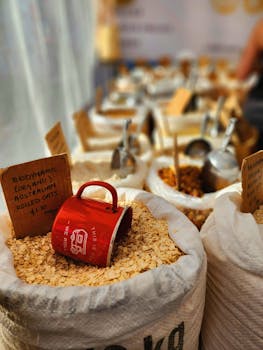 Bags of organic rolled oats in a market setting with a vibrant red mug captured in focus.