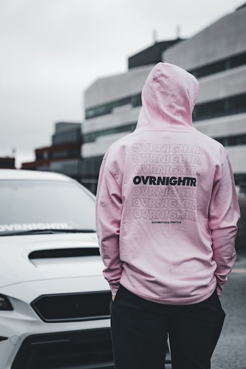 A man in a pink hoodie standing next to a car