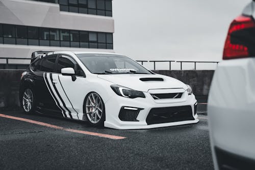 A white subaruna with black stripes parked in front of a building