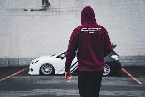 A man in a maroon hoodie walks past a car