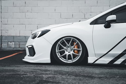 A white car with black rims parked in front of a building