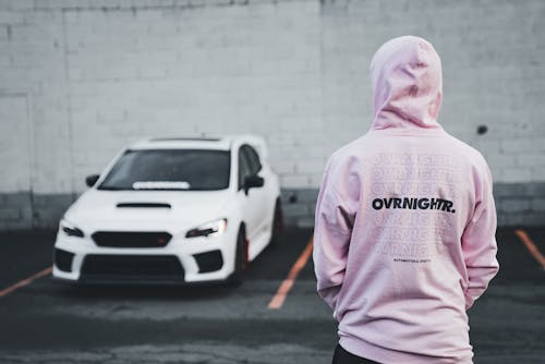 A person standing in front of a car wearing a pink hoodie