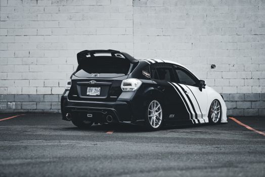 Back view of a customized black and white Subaru WRX sports car parked in an urban setting.