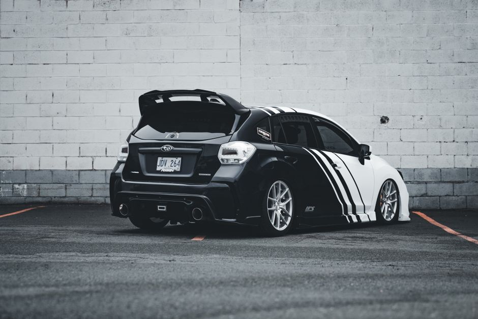 Back view of a customized black and white Subaru WRX sports car parked in an urban setting.