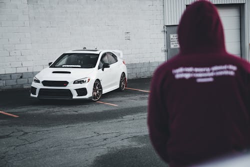 A person in a hoodie standing in front of a car