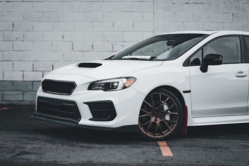 The white subaruna is parked in front of a brick wall