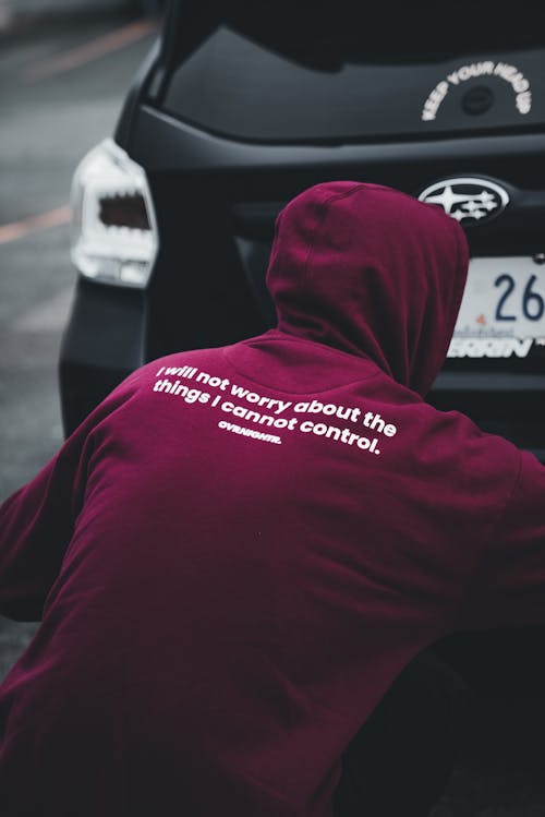 A man in a maroon hoodie leaning against a car