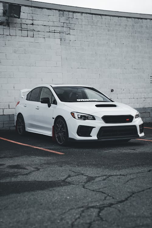 A white subaruna parked in front of a brick wall