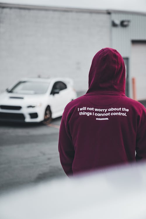 A man in a maroon hoodie standing in front of a car