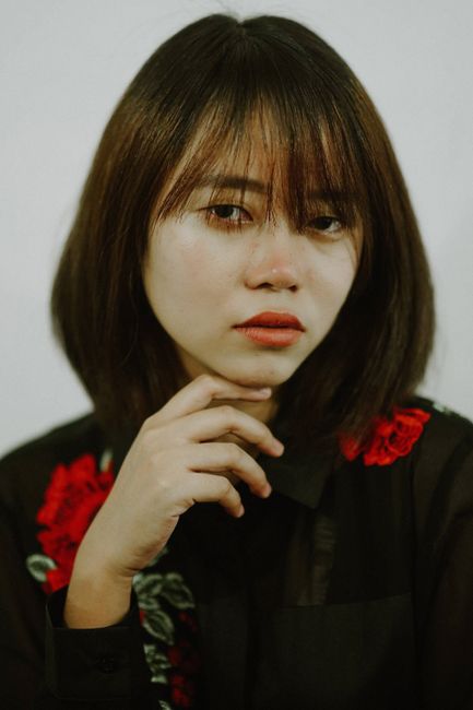 Elegant portrait of an Asian woman with serene expression and floral embroidered top, photographed i