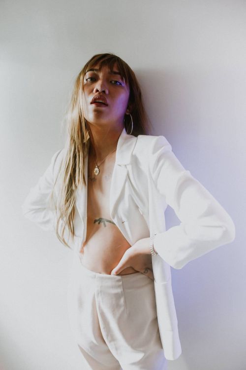 Free Fashion portrait of a woman with long hair in a white suit, striking a confident pose against a minimalistic background. Stock Photo
