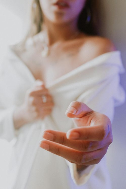 Free Close-up of a woman's hand reaching out in a fashion pose, wearing a white shirt. Soft and artistic touch. Stock Photo