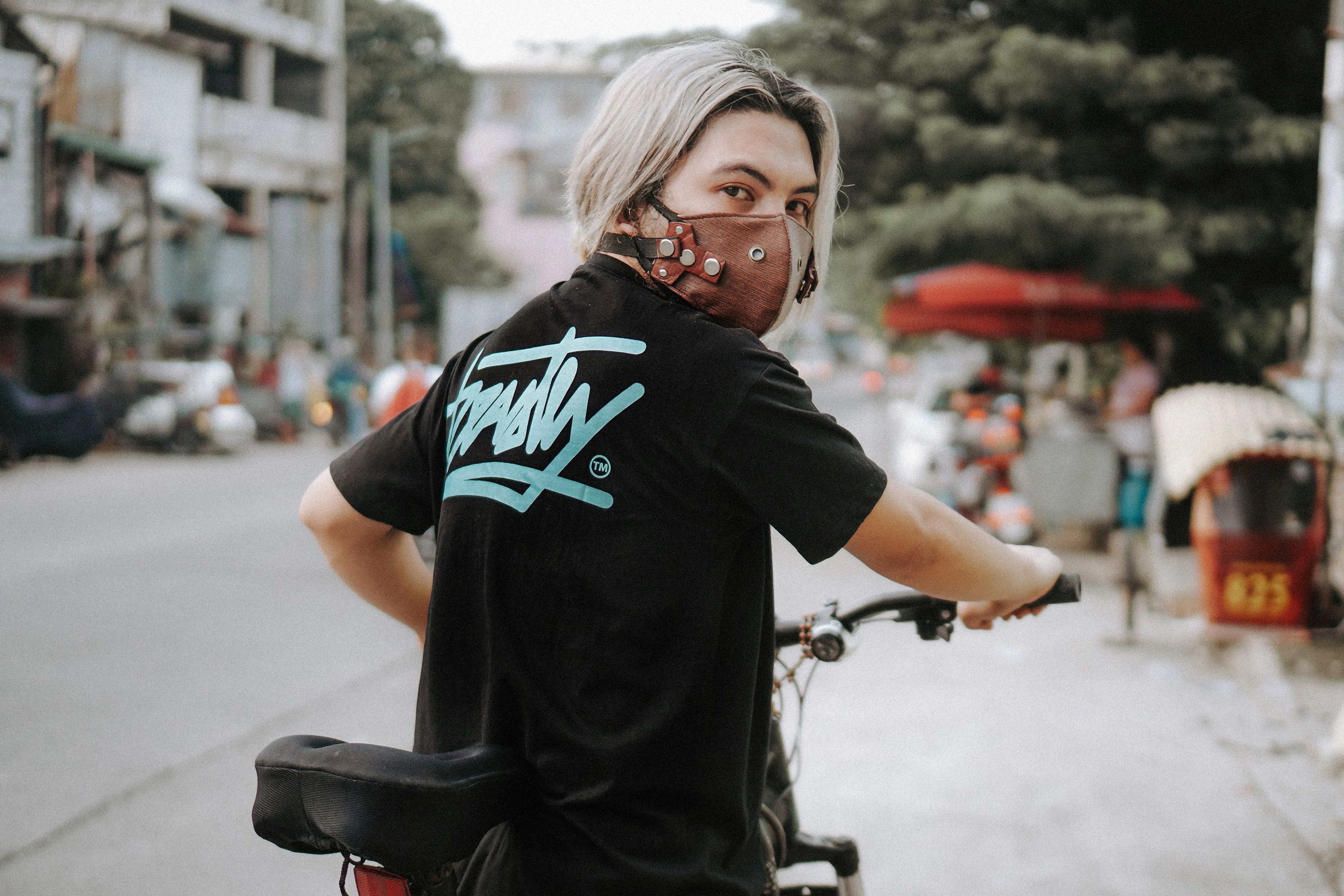 A young person in a face mask rides a bicycle through city streets, embodying urban lifestyle and safety.