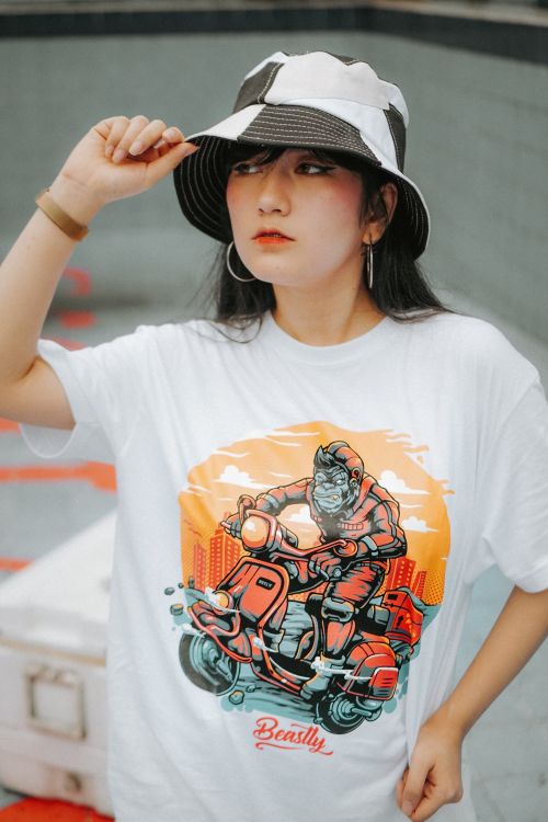 Free Young woman poses in a stylish graphic t-shirt and bucket hat outdoors. Stock Photo