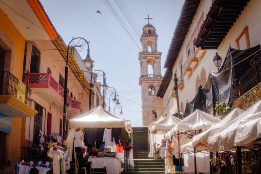 Vibrant outdoor market with church tower in Huauchinango, Mexico.