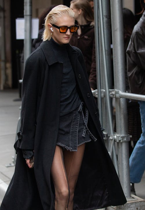 A woman in black coat and black stockings walking down the street