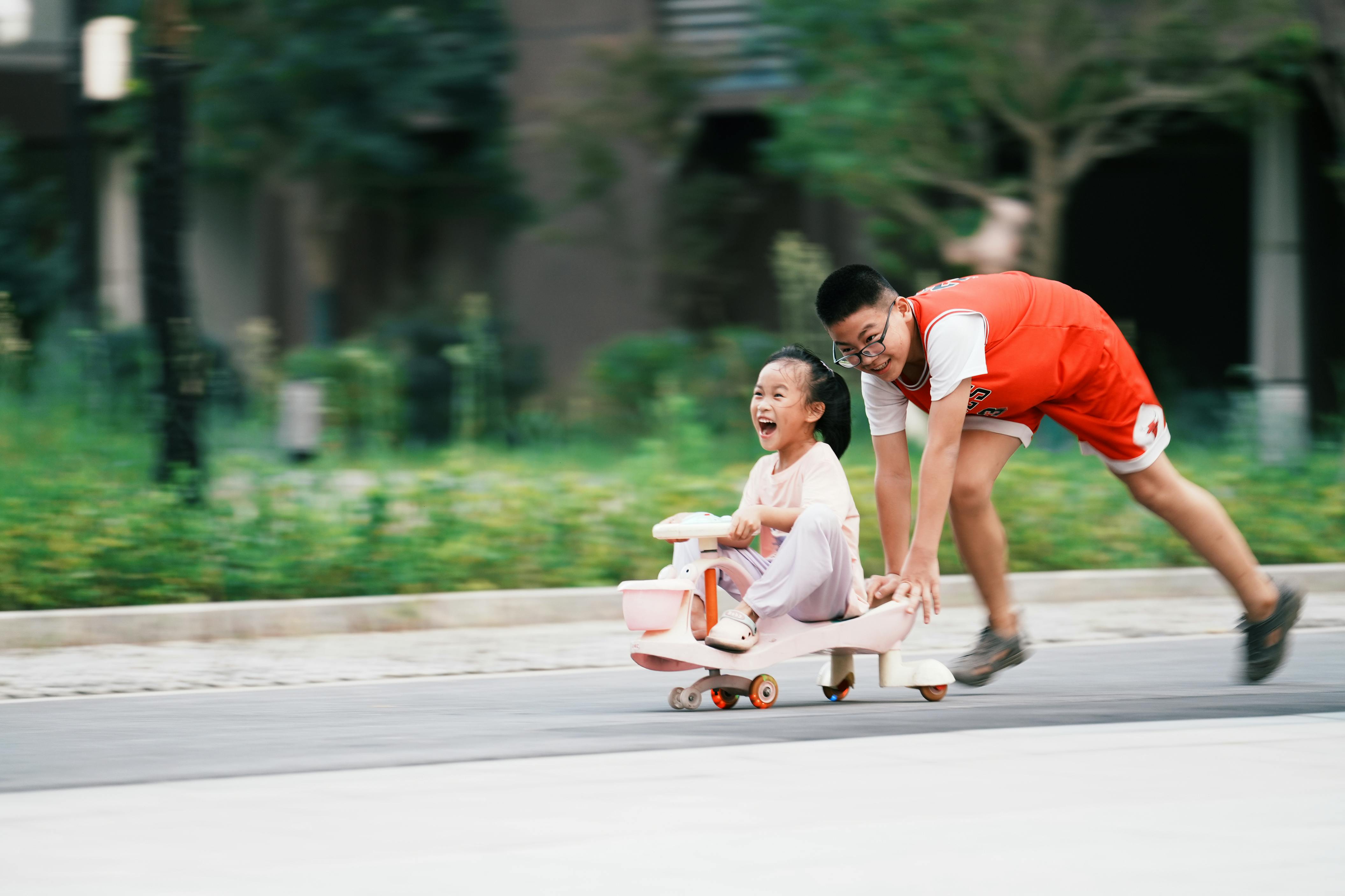 smiling brother pushing sister on toy with wheels