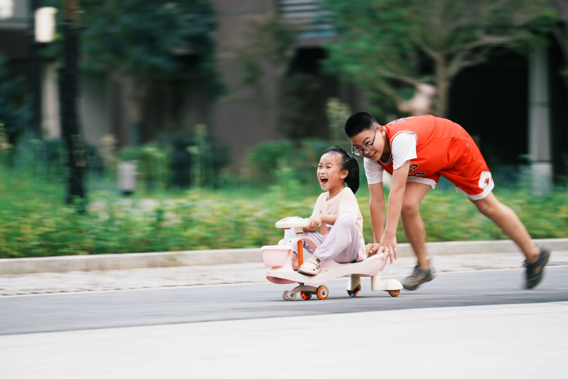 Smiling Brother Pushing Sister on Toy with Wheels