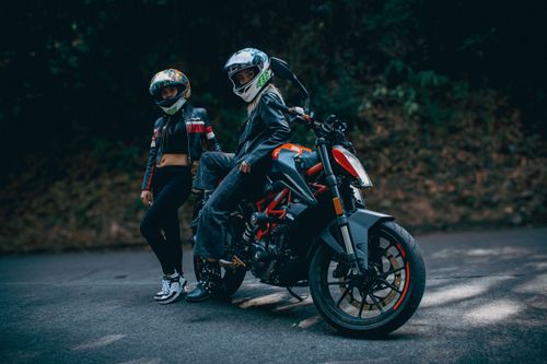 Free Two bikers wearing helmets and leather jackets posed with a KTM motorcycle on a rural road. Stock Photo