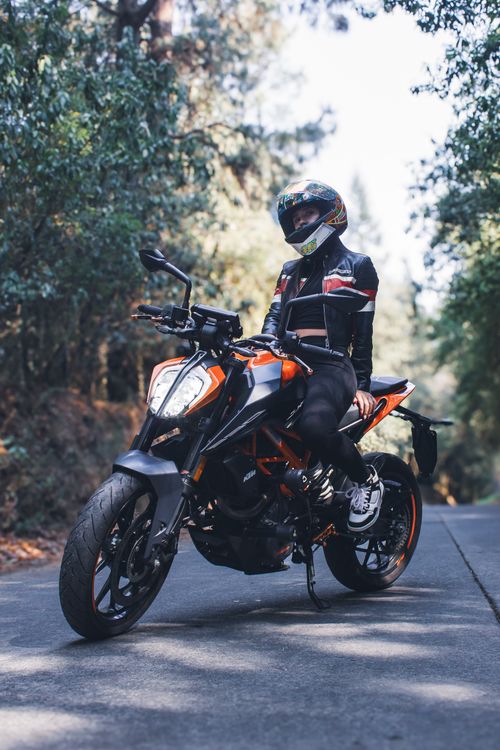 Free Woman sitting on a stylish motorbike in a forest, wearing a helmet and jacket. Stock Photo