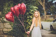 阳光明媚的户外，一位微笑的女子手拿红心气球