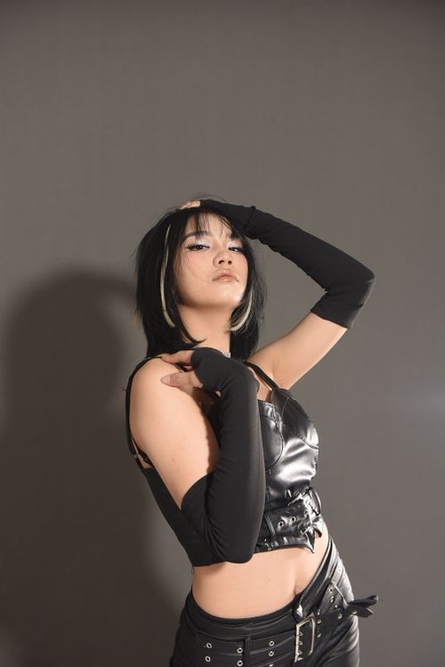 Free Fashion model in a black leather outfit poses confidently in a studio shoot with a gray background. Stock Photo
